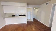 This single-floor space offers a practical and straightforward layout designed for comfortable everyday living. The open-concept living and kitchen area is anchored by rich, polished concrete floors that lend an industrial character to the interior, contrasting cleanly with the bright white walls and trim throughout.

The kitchen is defined by white shiplap-style cabinetry and a raised bar counter that separates it from the main living area. It is equipped with a white electric range and oven, a sink, and ample counter space. A dedicated utility area just beyond the kitchen houses a full-size white refrigerator set on light tile flooring, keeping the main living space visually uncluttered.

A hallway extends from the kitchen zone, leading to additional rooms within the unit. The corridor features a wall-mounted HVAC vent and thermostat, indicating a climate-controlled environment. The neutral, light grey wall tones throughout the space create a calm and cohesive atmosphere. The overall design is minimal and functional, with clean lines and a straightforward floor plan that maximizes usable space. The combination of polished concrete and white finishes gives the space a modern, utilitarian aesthetic well-suited to a variety of uses.