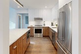 Located in the heart of Birmingham, Michigan, this sophisticated two-story residence offers 2 bedrooms and 3 bathrooms across two thoughtfully designed floors. The main level provides generous living space, anchored by a striking open-concept kitchen and living area. The chef's kitchen showcases a seamless blend of warm walnut lower cabinetry and high-gloss white upper cabinets, complemented by quartz countertops, a large island with seating, stainless steel appliances, and sleek linear pendant lighting — all set atop rich hardwood flooring that flows throughout the home. The living room is bathed in natural light through floor-to-ceiling windows that frame outdoor views and amplify the sense of openness. Soaring ceilings — particularly notable in the primary bedroom — lend a dramatic, airy quality to the upper level. The spacious primary bedroom features oversized windows overlooking a landscaped courtyard and benefits from a generous walk-in closet with built-in shelving. All three bathrooms are finished to a high standard, featuring large-format tile flooring, walnut vanities with quartz surfaces, and a glass-enclosed shower with full-height tile surround. The home's clean architectural lines, modern finishes, and abundant natural light combine to create an elevated and cohesive living experience.
