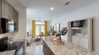This single-story residence in Bryan, Texas offers a well-designed open-concept floor plan that seamlessly connects the kitchen, dining, and living areas. The kitchen is a functional centerpiece, showcasing rich dark wood cabinetry, granite countertops, track lighting, and a generous island with bar seating—ideal for both meal preparation and casual dining. Black appliances, including a refrigerator, range, and built-in microwave, complement the contemporary cabinetry. Light wood-style flooring extends throughout the main living areas, adding warmth and continuity.

The living room is bright and inviting, featuring a ceiling fan, large windows, and glass doors that open to a private balcony, allowing natural light to fill the space. The bedroom accommodates a full-sized bed comfortably, with carpet flooring, a ceiling fan, and ample natural light from multiple windows with outdoor views. A second bedroom provides similar comfort and carpeted flooring. The bathroom features wood-look tile flooring, a vanity with granite countertops, and additional wall-mounted storage. A dedicated laundry area with a full-sized washer and dryer adds everyday convenience to this thoughtfully designed residence.