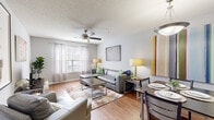 Located at Campus Pointe Circle in Gainesville, GA, this single-floor unit offers a well-organized layout designed for comfortable everyday living. The kitchen is equipped with warm oak cabinetry, light countertops, a double-basin sink, a black dishwasher, and a range, with a pass-through opening that connects seamlessly to the living and dining areas. Wood-style flooring runs throughout the main living spaces, adding warmth and continuity. The open living and dining area is bright and welcoming, featuring a ceiling fan, windows dressed with sheer curtains that allow generous natural light, and ample room for both lounging and dining. The dining space comfortably accommodates a full table and chairs. Each bedroom features plush carpeting, a ceiling fan, and sufficient space for a bed and desk setup, making them suitable for both rest and study. The bathroom is outfitted with a single-sink vanity with oak cabinetry, a full tub-shower combination, and wood-style flooring. Textured ceilings are present throughout, and neutral gray walls provide a clean, versatile backdrop across all rooms. The overall layout is practical and functional, offering a comfortable living environment in a residential community setting.