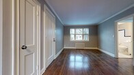 This single-floor residence offers a well-organized layout with a cohesive design aesthetic defined by rich, dark-stained hardwood flooring and cool gray-toned walls that run consistently throughout the space. Crown molding with crisp white trim adds a refined architectural detail to the living and bedroom areas, lending a classic character to each room.

The living area is generously proportioned, featuring multiple windows that allow natural light to fill the space, along with a traditional radiator that underscores the home's period charm. White panel doors and clean baseboards contribute to a polished, well-maintained interior.

The kitchen is outfitted with white shaker-style cabinetry — both upper and lower — paired with dark granite countertops and a stainless steel sink. A black Amana range anchors the cooking area, while an exposed brick accent wall adds texture and warmth to the room.

The bathroom retains a timeless vintage character, highlighted by white subway-style wall tiles accented with a dark border, a classic black-and-white mosaic tile floor, and a full soaking tub. A frosted window provides natural light while maintaining privacy.

Throughout the home, the combination of hardwood floors, traditional millwork, and neutral tones creates a cohesive and inviting living environment.