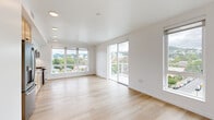 This thoughtfully designed 2-bedroom, 2-bathroom unit offers a clean, modern aesthetic across a single floor. Light hardwood flooring flows throughout the entire space, creating a sense of warmth and continuity.

The open-concept kitchen and living area serves as the heart of the unit. The kitchen is outfitted with stainless steel GE appliances — including a French door refrigerator, gas range, microwave, and dishwasher — complemented by natural wood lower cabinetry, white upper cabinets, a geometric tile backsplash, and grey countertops. Recessed lighting illuminates the space effectively. The adjacent living area is expansive and sun-drenched, featuring large picture windows and a sliding glass door that opens to a balcony with sweeping views of the surrounding urban landscape and tree-lined hills.

The primary bedroom is a comfortable, well-proportioned retreat with dual windows framing panoramic city and hillside views. The second bedroom also benefits from generous natural light and similar outdoor views. A dedicated closet provides additional storage.

The two bathrooms are finished with light wood vanities and grey countertops. One bathroom includes a soaking tub with shower. The hallways are bright and efficiently designed, with built-in cabinetry offering practical storage solutions. Overall, the unit presents a cohesive, contemporary feel throughout.