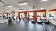 Located in Trinity, FL, this dedicated fitness center is designed to support a comprehensive workout experience. The single-floor facility is defined by bold red accent walls, white crown molding, and a durable rubber flooring surface that spans the entire space — practical for both cardio and strength training activity.

The cardio zone lines the windowed perimeter and features multiple treadmills, elliptical trainers, and stationary bikes, each equipped with individual digital displays. Wall-mounted flat-screen televisions are positioned throughout for entertainment during workouts. Large, shuttered windows along multiple walls flood the space with natural light while offering views of the surrounding outdoor landscape.

The strength training area houses a selection of cable and weight machines, a multi-tiered dumbbell rack with a full range of free weights, and additional resistance equipment. Full-length mirrors are mounted along one wall, enhancing the sense of openness and allowing users to monitor their form.

Overhead, ceiling fans with brushed metal finishes provide additional air circulation alongside the facility's ventilation system. Recessed and flush-mounted fluorescent lighting ensures consistent illumination throughout. The layout is open and well-organized, allowing for easy movement between equipment zones. Overall, the space delivers a clean, energetic, and fully functional environment suited for a wide range of fitness routines.