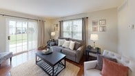 This thoughtfully designed single-floor residence offers a comfortable and cohesive living experience across a variety of well-appointed spaces. The living room serves as the heart of the home, featuring rich hardwood flooring, large windows with horizontal blinds and floor-length drape panels that invite an abundance of natural light, and a sliding glass door providing outdoor access. The adjacent dining area continues the hardwood flooring and is outfitted with a ceiling fan, chair rail molding, and a window overlooking the exterior. The galley-style kitchen is finished with white cabinetry, granite-style countertops, a double basin sink, and tile flooring, providing ample storage and workspace. Two well-sized bedrooms offer plush carpeting, generous window coverage, and walk-in closet access. The primary bedroom features a notably spacious layout with room for a seating area. Both bathrooms are finished with large-format tile flooring, white vanity cabinetry, granite countertops, and well-lit mirrors, presenting a clean and polished aesthetic. Throughout the residence, a neutral color palette of warm whites and soft grays creates a calm, cohesive ambiance that is both functional and inviting.