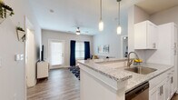 This single-floor residence is thoughtfully designed with a contemporary aesthetic, combining functionality and modern finishes throughout. The open-concept layout connects the kitchen directly to the living area, creating a seamless and social flow. The kitchen is a standout feature, equipped with white shaker-style cabinetry, stainless steel appliances, granite countertops, and a peninsula with pendant lighting overhead — ideal for casual dining or entertaining. Wood-look flooring runs consistently throughout the unit, lending warmth and visual continuity.

The dedicated dining area provides ample space for a full-sized table and seating, framed by a window that allows natural light to filter in. The living room benefits from a ceiling fan, additional windows, and access to an exterior door.

The bedrooms are well-proportioned, each featuring wood-look flooring, windows with natural light, and neutral wall tones that create a calm and restful atmosphere. The primary bathroom offers an elongated vanity with granite countertops, white cabinetry, and wood-look flooring, while a second bathroom provides a similarly refined vanity setup in a compact layout. The overall design maintains a clean, neutral palette with modern hardware and finishes throughout.