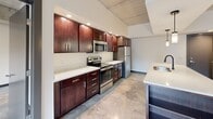Located at 112 Wayne Ave in Dayton, Ohio, this single-floor, 2-bedroom, 3-bathroom unit showcases a distinctly modern industrial aesthetic. Polished concrete floors run throughout the entire space, complementing exposed concrete structural columns and ceiling elements that lend an urban, loft-like character.

The kitchen serves as a central highlight, featuring rich dark wood cabinetry, white quartz countertops, stainless steel appliances, and a peninsula with a built-in sink and pendant lighting overhead. Recessed ceiling lighting and exposed concrete above the kitchen add further architectural interest.

Both bedrooms offer a clean, minimalist feel with natural light from black-framed windows that provide outdoor views of surrounding greenery. Each room includes a wall-mounted mini-split HVAC unit and ceiling fans for individual climate control. One bedroom features built-in white cabinetry for storage.

The three bathrooms are well-appointed, featuring polished concrete floors, rich wood vanities with white countertops, matte black fixtures, and either a tub-shower combination or an open walk-in shower. Dark-framed doors and consistent dark baseboards tie together the cohesive industrial-modern design throughout the unit.