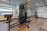 Located at 415 Clifford St in Detroit, Michigan, this single-floor fitness center offers a well-equipped workout environment designed for comprehensive exercise. The space features a mix of hardwood flooring and carpet tile throughout, lending a clean and modern aesthetic that blends industrial and contemporary design elements.

The main workout area is anchored by a multi-station strength training machine, complemented by cardio equipment including a stationary bike and an elliptical trainer. Free weights and weight plates are also available, along with an assortment of stability balls in multiple sizes, providing options for both strength and functional training.

Exposed ductwork and piping run along the ceiling, adding an industrial character to the space, while recessed and track lighting ensures the workout areas are well illuminated. A wall-mounted air conditioning unit supports climate control throughout the fitness floor.

A prominent dark-toned reception or check-in counter defines the entrance area, accented by warm pendant globe lighting that creates an inviting focal point. Adjacent to the reception, a long corridor lined with doors suggests access to additional amenities or private rooms. A window in one section of the space allows for natural light, enhancing the overall atmosphere. This fitness center is thoughtfully organized to support a variety of workout routines in a functional, well-maintained environment.