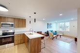 Located at 302 W Sixth St in downtown Chattanooga, Tennessee, this one-bedroom, one-bathroom unit offers a thoughtfully designed open-concept layout with a clean, modern aesthetic throughout. Light wood flooring flows seamlessly across the living, dining, and kitchen areas, creating a bright and cohesive atmosphere.

The kitchen is a standout feature, equipped with warm wood cabinetry, granite-style countertops, stainless steel appliances — including a refrigerator, range, and microwave — and a central island with bar seating and sleek pendant lighting overhead. The open layout connects the kitchen directly to the dining and living areas, making the space feel expansive and ideal for entertaining.

The living room is well-lit by a large window that brings in natural light and overlooks the surrounding cityscape. The bedroom also benefits from generous window views of downtown Chattanooga and the surrounding greenery, complemented by two closets for ample storage.

The bathroom features a full tub-shower combination with white tile surround, wood-toned vanity cabinetry, granite countertop, and light wood flooring that ties in with the rest of the unit. A rich wood-toned entry door adds a warm, welcoming touch at the entrance. The overall design is contemporary and cohesive, with a mid-century modern sensibility throughout.