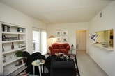 This single-floor residence offers a well-organized layout across several functional spaces. The living room serves as the central gathering area, featuring light carpet flooring, a textured ceiling, and built-in shelving that provides both display and storage space. Sliding glass doors open to a private balcony, allowing natural light to fill the room and offering outdoor views. A second seating angle confirms the balcony access and the presence of a front entry door, reinforcing the room's practical flow.

The galley-style kitchen is efficiently designed with white cabinetry accented by wood trim, a coil-top electric range, a full-size refrigerator, a dishwasher, and a sink. Upper cabinets extend to the ceiling, maximizing storage capacity. Tile-look flooring runs throughout the kitchen and continues into an adjacent utility or laundry area visible through a doorway.

Both bedrooms feature ceiling fans, carpet flooring, and textured ceilings. One bedroom includes a walk-in closet, providing ample storage. Windows in the bedrooms allow for natural light and ventilation.

The bathroom is equipped with a full tub and shower combination, a toilet, and a single-sink vanity with under-counter cabinetry. A wall-mounted medicine cabinet with mirror provides additional storage above the vanity area.