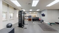 Located at 230 N 6th St in Richmond, Virginia, this fitness center offers a comprehensive exercise facility thoughtfully organized across a single, generously sized floor. The space is divided into distinct functional zones, each designed to support a well-rounded workout routine.

The cardio area features a row of modern treadmills equipped with individual screens, set against warm wood-toned flooring and accented by large mirrors with gold trim that enhance the sense of openness. Roller shades on the windows allow for adjustable natural light throughout the day.

The strength and free-weight zone is outfitted with a multi-use cable machine, adjustable benches, a dumbbell rack, stability balls, and kettlebells neatly stored on a dedicated shelf unit. Durable speckled rubber flooring throughout this section provides both safety and comfort during workouts.

The open layout also accommodates elliptical trainers and a rowing machine, complemented by wall-mounted flat-screen televisions for entertainment during exercise. Framed mirrors are strategically placed to support form-checking and to visually expand the space.

Bright recessed skylights and flush-panel ceiling lights ensure consistent, even illumination throughout the entire facility. The clean white walls and neutral color palette create a focused, energizing atmosphere well-suited for daily fitness activities.