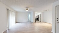 This single-floor residence presents a clean, neutral interior designed for comfortable everyday living. The open living and dining area serves as the heart of the home, featuring light-toned laminate flooring, a textured ceiling, and vertical blind-covered windows that allow natural light to filter through. A ceiling-mounted light fixture illuminates the space, which flows naturally toward a hallway connecting the remaining rooms.

The kitchen is notably updated, showcasing two-tone cabinetry with white uppers and grey lowers, white quartz countertops, a stainless steel undermount sink, and a tasteful subway tile backsplash in muted grey tones. Stainless steel appliances — including a range, microwave, and dishwasher — complete the functional and modern cooking space.

The bedrooms vary in flooring, with some featuring warm-toned laminate and others finished with neutral carpet. One bedroom offers dual louvered bi-fold closets providing generous storage, while another includes a standard reach-in closet. The bathroom area features light wood-look flooring, white cabinetry, and clean white walls. Throughout, the consistent use of white walls and light finishes creates a bright, cohesive ambiance.