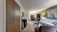This single-floor residence offers a thoughtfully designed layout that balances comfort and functionality. The entryway, framed by a warm wood-paneled door, opens into a spacious combined living and dining area where neutral walls, plush wall-to-wall carpeting, and an accent wall in muted taupe create a welcoming ambiance. The living room accommodates generous seating and is enhanced by natural light filtering through vertical blinds. Adjacent to the living space, the dedicated dining area features a pendant light fixture overhead and ample room for a round dining set, making it ideal for everyday meals or entertaining. The galley-style kitchen is outfitted with warm oak cabinetry, light countertops, a stainless steel sink, a range, and a dishwasher, offering a compact yet efficient workspace. Two well-proportioned bedrooms provide comfortable retreats, each featuring plush carpeting, vertical blinds for light control, and closet storage. One bedroom includes a spacious reach-in closet with a full rod system. The bathroom is cleanly finished with a tub-shower combination, a vanity with a dark wood cabinet base, and a well-lit mirror. Throughout the residence, the consistent use of neutral tones and soft textures contributes to a cohesive, calm aesthetic.