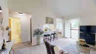 Located in Liverpool, NY, this 2-bedroom, 1-bathroom home offers a well-designed single-floor layout that maximizes comfort and functionality. The living room is a standout space, boasting dramatic vaulted ceilings that lend an open, airy feel far beyond its footprint. Soft carpeting and large sliding doors lead to a private balcony, flooding the room with natural light and outdoor views. A breakfast bar with seating connects the living area to the combined dining and kitchen space, creating a seamless flow ideal for everyday living and entertaining.

The kitchen features warm oak cabinetry extending to the ceiling, light tile flooring, a double sink, dishwasher, range, and refrigerator — offering ample storage and full functionality. The adjacent dining area includes a mirrored wall accent and large windows that bring in generous natural light.

Both bedrooms are carpeted and comfortably sized, each with windows that provide outdoor views and soft natural illumination. The primary bedroom offers a relaxing retreat with enough space for a full bedroom suite.

The bathroom is clean and well-appointed, featuring a tub/shower combination, an oak vanity with a single sink, a large mirror with overhead lighting, and light tile flooring consistent with the rest of the wet areas. A hallway connects all rooms efficiently, completing this practical and inviting home.