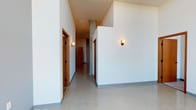 This single-floor unit showcases a contemporary architectural design characterized by notably high ceilings that lend an open, airy quality throughout. The interior hallway introduces the space with clean white walls, polished concrete floors, warm wood-toned doors, and understated wall sconces that provide a modern yet welcoming ambiance. Exposed concrete columns add an industrial touch to the corridor.

The kitchen is outfitted with dark espresso cabinetry, dark granite-style countertops, and a full suite of stainless steel appliances, including a refrigerator, range, microwave, and dishwasher. Polished concrete flooring continues here, complementing the sleek, modern aesthetic.

Multiple rooms feature soft carpeting and large floor-to-ceiling windows that flood the spaces with natural light while framing outdoor views of the surrounding landscape. The varied flooring—polished concrete in common areas and carpet in private rooms—provides functional distinction between spaces.

The bathrooms maintain the unit's modern design language, featuring dark vanity cabinetry, granite-style countertops, undermount sinks, and stone-look tile flooring. Chrome hardware and wall-mounted towel bars add clean finishing details throughout.