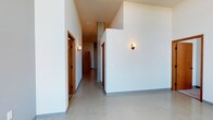 This single-floor unit showcases a contemporary architectural design characterized by notably high ceilings that lend an open, airy quality throughout. The interior hallway introduces the space with clean white walls, polished concrete floors, warm wood-toned doors, and understated wall sconces that provide a modern yet welcoming ambiance. Exposed concrete columns add an industrial touch to the corridor.

The kitchen is outfitted with dark espresso cabinetry, dark granite-style countertops, and a full suite of stainless steel appliances, including a refrigerator, range, microwave, and dishwasher. Polished concrete flooring continues here, complementing the sleek, modern aesthetic.

Multiple rooms feature soft carpeting and large floor-to-ceiling windows that flood the spaces with natural light while framing outdoor views of the surrounding landscape. The varied flooring—polished concrete in common areas and carpet in private rooms—provides functional distinction between spaces.

The bathrooms maintain the unit's modern design language, featuring dark vanity cabinetry, granite-style countertops, undermount sinks, and stone-look tile flooring. Chrome hardware and wall-mounted towel bars add clean finishing details throughout.