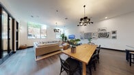 Located at 1916 Addison St in Berkeley, CA, this single-floor space offers an expansive, open-plan layout that seamlessly integrates a living area, dining zone, and kitchen. The interior is anchored by rich hardwood flooring that flows throughout, complemented by crisp white walls that lend a bright, airy atmosphere.

The living area is generously proportioned, featuring large sectional sofas arranged around upholstered ottomans and a low-profile media console with a wall-mounted TV. Oversized windows flood the space with natural light and offer views of the street, while striking sputnik-style chandeliers add a bold, contemporary focal point overhead. A curated gallery wall of framed artwork adds visual depth and personality.

The dining area centers on a substantial natural wood communal table surrounded by black Windsor-style chairs, positioned beneath another statement chandelier. A gallery wall of eclectic framed prints lines the adjacent wall, adding an artistic layer to the space.

The kitchen is defined by matte black cabinetry, white subway tile backsplash, stainless steel appliances, and a striped stone-topped island. Floating black shelves display an artful collection of baskets, books, and ceramics, reinforcing the space's curated aesthetic. Floor-to-ceiling glass partitions divide areas while maintaining visual continuity throughout.