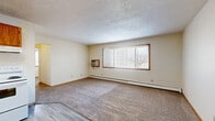 Located at 1209 20th St S in Moorhead, Minnesota, this single-floor residence offers a practical and straightforward layout encompassing three bedrooms, one bathroom, a living room, kitchen, and hallway. The open living area transitions seamlessly from the kitchen, where warm oak cabinetry surrounds a white electric range and refrigerator, complemented by light wood-style flooring. The living room is generously proportioned, featuring large windows with vertical blinds that allow abundant natural light, baseboard heating, and a wall-mounted air conditioning unit for year-round comfort. A textured ceiling adds a classic finishing detail throughout the main living space. Each of the three bedrooms is carpeted and features windows with views to the outdoors, along with baseboard heating. Several bedrooms include sliding or bi-fold closets, providing practical storage solutions. The primary bedroom is a comfortable, well-lit space with natural light filtering through large windows. The full bathroom is efficiently designed with light wood-style flooring, a pedestal sink, mirror with overhead lighting, toilet, and a shower-tub combination. A connecting hallway links the bedrooms and bathroom, completing this functional and well-organized floor plan.