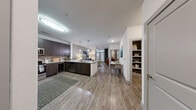 This well-appointed single-floor residence offers a thoughtfully designed open-concept layout that seamlessly connects the kitchen, dining, and living areas. The kitchen is a standout feature, showcasing dark espresso cabinetry, stainless steel appliances including a refrigerator, range, and microwave, a tiled backsplash, and a peninsula with granite-style countertops and pendant lighting overhead. A beverage cooler adds a refined touch to the space.

Wood-look plank flooring runs throughout the main living areas, lending warmth and cohesion to the open floor plan. The living room is bright and inviting, anchored by a large sliding glass door that opens to an outdoor area and floods the space with natural light. A ceiling fan adds comfort overhead.

The dining area sits conveniently between the kitchen and living room, creating a natural flow for everyday living and entertaining. Two well-sized bedrooms offer plush carpeting, ceiling fans, and large windows with outdoor views. The primary bedroom benefits from a generously sized walk-in closet complete with built-in shelving and hanging rods, offering ample organized storage. A dedicated built-in bookshelf nook near the entry provides additional functional storage. The overall ambiance is clean, contemporary, and move-in ready.
