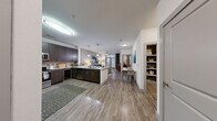 This well-appointed single-floor residence offers a thoughtfully designed open-concept layout that seamlessly connects the kitchen, dining, and living areas. The kitchen is a standout feature, showcasing dark espresso cabinetry, stainless steel appliances including a refrigerator, range, and microwave, a tiled backsplash, and a peninsula with granite-style countertops and pendant lighting overhead. A beverage cooler adds a refined touch to the space.

Wood-look plank flooring runs throughout the main living areas, lending warmth and cohesion to the open floor plan. The living room is bright and inviting, anchored by a large sliding glass door that opens to an outdoor area and floods the space with natural light. A ceiling fan adds comfort overhead.

The dining area sits conveniently between the kitchen and living room, creating a natural flow for everyday living and entertaining. Two well-sized bedrooms offer plush carpeting, ceiling fans, and large windows with outdoor views. The primary bedroom benefits from a generously sized walk-in closet complete with built-in shelving and hanging rods, offering ample organized storage. A dedicated built-in bookshelf nook near the entry provides additional functional storage. The overall ambiance is clean, contemporary, and move-in ready.