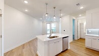 Located at 1 Riverside Ave in Jacksonville, FL, this modern one-bedroom, one-bathroom unit offers a thoughtfully designed open-concept layout with clean lines and a bright, contemporary aesthetic throughout. Light hardwood flooring flows seamlessly across the entire space, complementing the crisp white walls and recessed lighting that keep the interior feeling fresh and airy.

The combined kitchen and living area serves as the heart of the unit. The kitchen is equipped with a full suite of stainless steel appliances, including a refrigerator, range, microwave, and dishwasher. A central island with a white quartz countertop and an undermount sink doubles as a casual dining and prep space, elegantly lit by a trio of globe pendant lights suspended from the ceiling. White shaker cabinetry and a soft blue-grey subway tile backsplash complete the kitchen's polished look.

The bedroom offers a comfortable, well-lit retreat with a large window and a glass door providing access to a balcony with outdoor views. A generously sized walk-in closet outfitted with wire shelving and organizational racks adds practical storage. The bathroom features a white vanity with quartz countertop, a framed mirror, and a shower-tub combination. The unit also includes an in-unit laundry area, rounding out a well-appointed and efficiently designed living space.