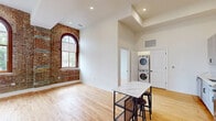 Located at 179 Chelsea Ave in Long Branch, NJ, this 2-bedroom, 1-bathroom unit masterfully blends historic character with modern updates. The living area is immediately distinguished by dramatic exposed brick walls and striking arched windows that flood the space with natural light, all complemented by warm hardwood flooring throughout. High ceilings amplify the sense of openness, creating an airy and inviting atmosphere.

The kitchen is outfitted with sleek gray cabinetry, marble-look quartz countertops, stainless steel appliances including a refrigerator, range, microwave, and dishwasher, and a modern matte black faucet. A marble-top island with bar seating provides additional workspace and casual dining. Conveniently tucked nearby is an in-unit stacked washer and dryer.

The bedrooms continue the exposed brick and hardwood aesthetic, with the primary bedroom featuring a pair of arched windows that offer views of the surrounding neighborhood. The second bedroom is bright and clean with crisp white walls.

The bathroom is finished with large-format tile flooring, a white vanity with quartz countertop, and a glass-enclosed walk-in shower adorned with marble-look tile walls and a mosaic tile floor, providing a polished, spa-like feel.