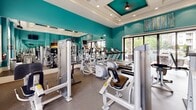 Located at 4600 Pear Grove Ct in Glen Allen, Virginia, this single-level fitness center is designed to support a comprehensive workout experience. The space is immediately distinguished by its vibrant teal walls, which are complemented by crisp white trim and elegantly coffered ceilings with recessed lighting and ceiling fans—lending the room a polished, upscale character.

The fitness floor is outfitted with a wide array of modern equipment, including Precor cardio machines such as ellipticals and treadmills, as well as a full selection of strength-training stations and cable machines. A dedicated free weights area features a dumbbell rack alongside an adjustable bench, accommodating a range of training preferences. Full-length mirrors line the walls, visually expanding the space and allowing exercisers to monitor their form throughout their sessions. Wall-mounted flat-screen televisions provide entertainment during workouts.

Natural light flows generously through large windows and expansive sliding glass doors, which open directly to an outdoor patio area featuring stone columns and views of a pool. Durable rubber flooring throughout ensures both safety and comfort. An adjacent room, visible through an interior doorway, suggests additional amenity space nearby. The overall ambiance is energetic yet refined, making this fitness center a functional and attractive facility.