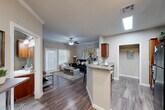 Located in Tomball, TX, this well-appointed 2-bedroom, 2-bathroom residence offers a thoughtfully designed single-floor layout that maximizes comfort and functionality. The open-concept living and kitchen area serves as the heart of the home, where rich wood-toned cabinetry, granite countertops, and a wraparound breakfast bar create an inviting space for cooking and entertaining. A skylight above the kitchen enhances natural brightness, while track lighting and crown molding add refined detail. Black appliances, including a refrigerator, range, and microwave, complement the kitchen's warm aesthetic. Wood-style plank flooring flows throughout the main living areas, transitioning to plush carpet in the bedrooms. The living room features crown molding, a ceiling fan, and large windows that invite ample natural light, with access to an exterior door. The primary bedroom includes its own walk-in closet and an en-suite bathroom with granite vanity, wood cabinetry, and a tiled tub-shower combination. The second bedroom is comfortably sized with a ceiling fan and generous window. A dedicated laundry area with full-size washer accommodates everyday convenience. Two closets provide ample storage throughout the residence.