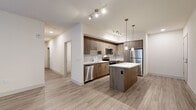 Located at Bear Creek Way NE in Redmond, WA, this single-floor residence showcases a thoughtfully designed modern interior with a cohesive aesthetic throughout. The kitchen serves as a standout feature, offering wood-toned cabinetry extending to the ceiling, a geometric tile backsplash, and a full suite of stainless steel appliances including a refrigerator, range, microwave, and dishwasher. A central island with a white quartz countertop provides additional workspace and casual seating, while pendant lighting and track lighting illuminate the space effectively. Light wood-look flooring flows throughout the main living areas, creating a warm, unified feel. The bedrooms are finished with plush carpeting and ceiling fans, with natural light entering through large windows fitted with horizontal blinds. One bedroom offers direct access to an outdoor area via a sliding glass door. A walk-in closet with wire shelving and hanging rods adds practical storage. The bathroom features subway tile surrounding a soaking tub and shower combination, complemented by tile flooring. A dedicated laundry area with a full-size washer and dryer rounds out the functional, well-planned layout.