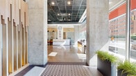 Located at 947 N Park Ave in Tucson, Arizona, this contemporary single-floor commercial space offers an expansive and thoughtfully designed environment with a distinctly modern architectural character. The grand entrance lobby immediately impresses with its polished concrete floors, exposed concrete columns, and a dark grid ceiling with recessed lighting that creates a striking industrial-modern aesthetic. Floor-to-ceiling windows flood the reception area with abundant natural light while framing views of the surrounding Tucson streetscape, including palm trees and the urban corridor beyond.

The reception zone features a sleek white service counter complemented by warm wood accents and pendant lighting, establishing a professional and welcoming first impression. Adjacent spaces include a spacious lounge and social area outfitted with a full-size pool table, comfortable seating arrangements, a wall-mounted display, and vibrant wall murals that energize the environment. A separate community lounge with warm wood flooring, slatted wood ceilings, and abundant seating offers a relaxed gathering atmosphere with views to the exterior.

Multiple private conference rooms provide intimate settings for meetings, each furnished with wood conference tables, upholstered chairs, display screens, and glass partition walls. A dedicated mailroom area with a wood-trimmed service counter and built-in mailboxes adds functional convenience. Throughout the space, a cohesive palette of concrete, wood, and clean white surfaces creates a polished, contemporary ambiance.