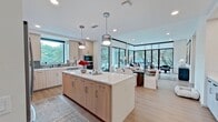 This thoughtfully designed single-story residence spans 1,620 square feet and features 3 bedrooms, 5 bathrooms, 4 closets, a dedicated laundry room, and 2 hallways. The living room is a standout space, anchored by expansive floor-to-ceiling black-framed windows that flood the interior with natural light and offer sweeping views of mature trees and the surrounding landscape. The kitchen is outfitted with light wood cabinetry, a large white quartz island with bar seating for three, a tile backsplash, stainless steel appliances, pendant lighting, and a built-in wine refrigerator. The primary bedroom measures 190 square feet and connects to a well-appointed en-suite bathroom featuring light tile flooring, a long vanity with gray cabinetry, an LED-lit mirror, and direct access to a custom walk-in closet with adjustable shelving and hanging systems. Additional bedrooms are bright and well-proportioned, each with hardwood-style flooring and natural light. The laundry room includes a full-size front-load washer and shelving for storage. Throughout, the home maintains a clean, neutral palette with white walls, recessed lighting, and modern finishes, creating a cohesive and contemporary living environment.