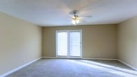 This single-floor space offers a clean, functional layout designed for comfortable everyday living. The main living area is finished with soft wall-to-wall carpeting and features neutral, warm-toned walls that create a welcoming and versatile backdrop for any furnishing style. A sliding glass door serves as a prominent architectural feature, flooding the room with generous natural light and providing convenient access to the outdoors. The ceiling is finished with a classic textured treatment and is equipped with a ceiling fan with an integrated light kit, supporting both comfort and airflow year-round. Clean white baseboards and trim provide a crisp contrast to the warm wall tones, adding a polished, cohesive look throughout. The open, unobstructed layout of the living space allows for flexible furniture arrangements to suit a variety of needs. Overall, the space presents a bright, airy ambiance with practical finishes and functional design elements that make it move-in ready and easy to personalize.