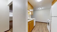 Located at 3050 Old Highway 8 in Roseville, MN, this 2-bedroom, 1-bathroom unit offers a straightforward single-floor layout designed for comfortable everyday living. The kitchen features warm oak cabinetry — both upper and lower — paired with a double-basin sink, a dishwasher, and durable wood-look plank flooring, all framed by a textured accent wall that adds subtle visual interest. The layout connects the kitchen to the living area, which continues the wood-style flooring before transitioning into carpeted spaces throughout the rest of the unit. The generously sized primary bedroom is a standout feature, offering ample square footage along with dual built-in closets that provide substantial storage. A window unit provides in-room climate control, and a baseboard heating system runs along the exterior wall. The second bedroom is also carpeted, features a window with blinds for natural light and privacy, and includes its own baseboard heating. The full bathroom is clean and functional, with floor-to-ceiling white tile surrounding a full soaking tub and shower combination. A connecting hallway ties the rooms together efficiently. Neutral tones, including white walls and beige carpet, create a clean and versatile interior throughout the unit.