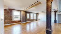 Located in the heart of downtown Houston at 909 Texas Ave, this single-floor loft masterfully blends historic industrial character with modern updates. The expansive open main area showcases original exposed brick walls, warm hardwood floors, and prominent wood ceiling beams supported by cast-iron columns — all hallmarks of the building's storied architectural heritage. Multiple large windows line the brick walls, bathing the interior in generous natural light while offering elevated views of the surrounding Houston skyline.

The kitchen is thoughtfully designed with two-tone cabinetry, white subway tile backsplash, stainless steel appliances, and a center island with pendant lighting — ideal for both everyday cooking and entertaining. The bathroom combines modern and vintage sensibilities, featuring a freestanding soaking tub, a double vanity with blue cabinetry, and exposed brick accents. An adjacent laundry area with stacked washer and dryer adds everyday convenience. A dedicated walk-in closet with built-in shelving and wire racking provides ample storage, finished with polished concrete flooring. Utility rooms and a defined entrance round out the well-organized layout, making this loft a distinctive urban retreat.