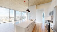 Located in Chicago's vibrant West Loop neighborhood, this modern 3-bedroom, 2-bathroom residence offers a thoughtfully designed open layout with high-end finishes throughout. The combined kitchen and living area serves as the heart of the home, showcasing exposed concrete ceilings, warm hardwood flooring, and dramatic floor-to-ceiling windows that flood the space with natural light and frame sweeping panoramic views of the Chicago skyline and cityscape. The kitchen is equipped with stainless steel appliances, including a gas range, microwave, and full-size refrigerator, complemented by sleek white cabinetry, a tiled backsplash, and a generous island with a white quartz countertop and black hardware accents. The primary bedroom is a well-proportioned retreat featuring expansive corner windows with unobstructed city views. Additional bedrooms are bright and well-sized, each with hardwood flooring. The two bathrooms are finished with large-format tile flooring, modern vanities with integrated sinks, matte black fixtures, and illuminated mirrors. Two organized closets provide ample storage, and an in-unit laundry area adds everyday convenience. The residence's elevated position enhances its open, airy ambiance throughout.