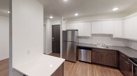 This thoughtfully designed single-floor unit offers a clean, modern aesthetic throughout. The open-concept kitchen is a standout feature, equipped with stainless steel appliances including a refrigerator, dishwasher, electric range, and over-the-range microwave. White upper cabinetry contrasts elegantly with dark lower cabinets, complemented by grey countertops and a classic white subway tile backsplash. A peninsula island adds additional prep and storage space, while light wood-style flooring ties the kitchen and adjacent living area together seamlessly.

The living area is bright and spacious, featuring sliding glass doors that open to a private balcony overlooking greenery, bringing in natural light and outdoor views. A wall-mounted HVAC unit and baseboard heating provide year-round climate comfort.

The bedrooms are carpeted for warmth and comfort, each featuring ceiling fans with lighting and windows with blinds. One bedroom includes a wall-mounted unit for additional climate control.

Two bathrooms serve the unit. One features dark large-format floor and shower surround tiles with a soaking tub, dark wood vanity, and wall-mounted cabinet. The second bathroom offers a lighter, more minimalist design with grey tile flooring, a white vanity, and a wall-mounted storage cabinet. Both bathrooms are finished with chrome fixtures and clean white walls.
