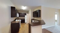This single-story residence at Parks At Vine is thoughtfully designed with a practical, open layout that connects the main living and kitchen areas seamlessly. The kitchen is a standout feature, equipped with rich dark espresso cabinetry offering generous storage, dark laminate countertops, wood-look flooring, and white appliances including a range, refrigerator, and built-in microwave. A peninsula with an integrated sink and additional upper cabinetry defines the boundary between the kitchen and the open living space, which transitions between hardwood-style flooring and plush carpet.

The expansive living area includes a ceiling fan with light fixture and French doors that invite natural light while providing access to the exterior. Bedrooms are carpeted and feature warm neutral-toned walls, natural light from double windows, and ceiling fans for added comfort. Additional rooms offer similar carpeted finishes and natural light.

The bathroom includes a full-size soaking tub and shower combination with clean white surroundings and tile flooring. A dedicated laundry area with wire shelving and washer/dryer hookups adds functional convenience. Throughout the residence, the neutral color palette and consistent finishes create a cohesive, comfortable living environment.