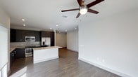 This single-story space in Plano offers an open-concept design that seamlessly connects the kitchen and living areas, creating a cohesive and functional layout. The kitchen is outfitted with dark espresso cabinetry that provides a striking contrast against the light-toned countertops and tile backsplash. A peninsula with a white base serves as a natural divider between the kitchen and the living space, offering additional prep and seating potential. Stainless steel appliances, including a French door refrigerator and built-in microwave, add a polished, contemporary feel. Recessed lighting throughout the kitchen and living area ensures consistent, well-distributed illumination, complemented by a ceiling fan with a light fixture in the main living space that enhances both comfort and airflow. The wood-style flooring extends across the entire open area, adding warmth and visual continuity. Clean white walls and a neutral color palette create a bright, airy atmosphere, while the open sightlines between rooms contribute to a spacious, welcoming ambiance suited to both everyday living and entertaining.
