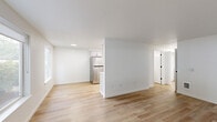 This single-story, 2-bedroom, 1-bathroom unit offers a thoughtfully designed layout with a clean, modern aesthetic throughout. Light hardwood flooring runs continuously across all rooms, complementing the crisp white walls and creating a bright, cohesive feel.

The open-concept living and kitchen area serves as the heart of the unit. The kitchen is well-appointed with white shaker-style cabinetry featuring matte black hardware, white countertops, stainless steel appliances including a refrigerator and range, and a skylight that draws in additional natural light. A partial dividing wall subtly separates the kitchen from the living area while maintaining an open, airy flow.

The primary bedroom is generously sized, offering ample space and connecting to a hallway that leads to the rest of the unit. The second bedroom features a window with a green outdoor view, providing natural light and a pleasant outlook. Both bedrooms include built-in closet storage with sliding doors.

The bathroom is finished in a minimalist style, with white cabinetry, a white countertop vanity with matte black hardware, a bathtub with shower, and matching hardwood-style flooring that ties the space together. A hallway connects all rooms, completing the efficient and functional floor plan.
