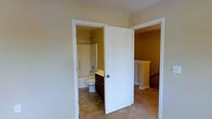 This two-story home at Cave Mill is designed with functional living in mind. The upper level reveals a well-arranged layout, highlighted by a full bathroom equipped with a combination tub and shower, a dark-stained wood vanity with storage, and tile flooring. The bathroom is accessible via a classic six-panel white door, a design detail that carries throughout the home and contributes to a clean, traditional aesthetic. Neutral-toned carpet flows through the upper-level rooms, complementing the warm, golden wall tones that give the space a welcoming atmosphere. A staircase with a decorative newel post connects the two floors, featuring elegant detailing that adds architectural character to the interior. The white trim and baseboards throughout provide crisp contrast against the warmer wall colors, reinforcing the home's cohesive style. The layout appears thoughtfully arranged, offering practical separation between living and private spaces across the two floors. Overall, the home presents a comfortable and classic interior with consistent finishes and traditional design elements.