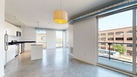 Located at 915 Washington Ave N in Minneapolis' vibrant North Loop neighborhood, this 2-bedroom, 2-bathroom unit showcases a contemporary industrial aesthetic throughout. Polished concrete floors and exposed silver ductwork run the length of the open-plan living space, lending an authentic urban loft character. Large floor-to-ceiling windows flood the interior with natural light while framing views of the surrounding cityscape, and a sliding glass door opens to a private balcony.

The kitchen is well-appointed with white cabinetry, dark countertops, stainless steel appliances including a refrigerator, range, microwave, and dishwasher, and a central island that doubles as a breakfast bar. Track lighting overhead adds both functionality and style. A stacked in-unit washer and dryer is conveniently tucked nearby.

The generously sized primary bedroom offers ample space and built-in wardrobe storage, while the second bedroom benefits from its own large window and concrete flooring. Two full bathrooms serve the unit — one featuring a clean walk-in shower, the other a full soaking tub and shower combination with tile flooring. The overall ambiance is bright, clean, and modern, ideal for urban living.