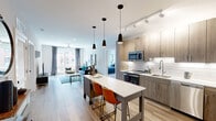 This well-appointed 2-bedroom, 2-bathroom residence delivers a cohesive modern aesthetic across a single-level, open-concept floor plan. Light hardwood flooring flows throughout the main living areas, anchoring a seamless connection between the kitchen, dining, and living spaces.

The kitchen is a standout feature, showcasing wood-toned cabinetry, a classic white subway tile backsplash, quartz countertops, and a full suite of stainless steel appliances. A central island with seating provides additional prep space and a natural gathering point. Pendant lighting and track lighting add layered illumination throughout.

The living room is bright and airy, benefiting from large windows that bring in generous natural light and views of the surrounding urban streetscape. A ceiling fan adds comfort to the open space.

The primary bedroom is generously sized, featuring large windows with outdoor views and plush carpeting. It connects to a dedicated bathroom and a spacious walk-in closet with full wire shelving systems. The second bedroom is versatile, with its own adjacent bathroom featuring a glass-enclosed walk-in shower and clean tile finishes.

Both bathrooms are finished with floating wood vanities, backlit mirrors, and crisp white countertops. Two closets provide ample storage throughout the residence, rounding out a well-organized and functional layout.