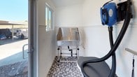 This dedicated pet parlor is a thoughtfully designed grooming space built to accommodate the care and comfort of pets. The room centers around a large, professional-grade stainless steel grooming tub complete with an integrated spray hose and accessory shelf, making bath time efficient and thorough. A wall-mounted pet dryer with flexible hose attachments is conveniently positioned nearby, ensuring a streamlined grooming workflow from wash to dry. A separate grooming table with an anti-slip surface and restraint arm provides a dedicated area for finishing touches. The interior walls are finished with clean white subway tile wainscoting paired with smooth white paint above, creating a bright, hygienic, and easy-to-clean environment. Underfoot, a classic hexagonal mosaic tile floor adds both a stylish touch and practical durability. Natural light filters in through windows, keeping the space feeling open and fresh. A full-light glass door opens directly to an outdoor courtyard, offering convenient access for pets and their owners. This single-level space is designed with functionality and cleanliness in mind, making it an ideal amenity for pet owners.