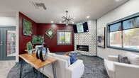 Located at 1333 N Dysart Rd in Avondale, Arizona, this single-floor community lounge space offers a thoughtfully designed open-plan layout combining a kitchen and living area. The living area makes a bold visual statement with a deep crimson accent wall adorned with living wall art panels, adding a vibrant, biophilic touch to the interior. A sleek tiled fireplace serves as a focal point, framed by a geometric Moroccan-style tile surround, with a wall-mounted television above. Comfortable white sofas and accent chairs are arranged around a contemporary glass coffee table, all set atop patterned carpeting. A striking sputnik-style chandelier and recessed lighting illuminate the lounge area.

The kitchen zone features teal-toned cabinetry with crisp white countertops, open industrial-style shelving mounted against a textured wave-pattern accent wall, and a built-in beverage refrigerator. Light wood-look flooring grounds the kitchen, while pendant lighting and a breakfast bar with modern seating create a welcoming social atmosphere. Large windows throughout offer views of lush palm trees and a pool area, filling the space with natural light. A sliding barn door adds a functional yet stylish architectural detail to the overall design.