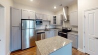 This single-floor residence at 919 Woody Dr in Graham, NC offers a thoughtfully designed layout with modern finishes throughout. The open-concept living area welcomes you upon entry, featuring rich hardwood-style flooring, neutral walls, and a ceiling fan with a built-in light fixture. Large windows allow natural light to fill the space, creating a warm and inviting atmosphere.

The kitchen is a standout feature, equipped with gray shaker-style cabinetry, granite countertops, and a full suite of stainless steel appliances including a refrigerator, electric range, built-in microwave, and dishwasher. A wall-mounted range hood adds a contemporary touch, while a center island with matching granite provides additional prep and dining space. Hardwood-style flooring continues seamlessly from the living area into the kitchen.

The bedroom offers plush carpet flooring, a ceiling fan, and windows with blinds that bring in natural light. The bathroom is well-appointed with hardwood-style flooring, a granite-topped vanity with dual sinks, and a tub-shower combination with subway tile surround. Clean white walls and recessed lighting contribute to the space's bright, modern aesthetic throughout.