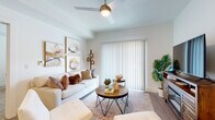 This single-story residence is thoughtfully designed with a consistent, modern aesthetic carried throughout each space. The living area serves as the heart of the home, featuring wood-style flooring, a ceiling fan with integrated lighting, and a sliding glass door dressed with vertical blinds that allows natural light to fill the room. The open layout flows naturally into the kitchen, which is outfitted with dark espresso cabinetry, granite-look countertops, a stainless steel appliance suite including a gas range, over-the-range microwave, and refrigerator, and light wood-style flooring that complements the clean, contemporary feel.

The bedroom is a calm retreat with plush carpeting, a generous window with blinds and curtain panels, and ample natural light. A versatile secondary room with carpeted flooring and a window offers flexible use as a home office or additional living space. Both bathrooms maintain the same design language as the kitchen, featuring espresso vanity cabinetry, granite-look countertops, large mirrors, and wood-style flooring. The overall ambiance of the residence is bright and cohesive, with white walls and modern finishes creating a welcoming, move-in-ready environment.