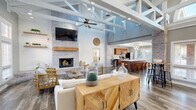 Located in Perrysburg, Ohio, this thoughtfully designed single-floor space makes a striking first impression with its dramatic vaulted ceilings adorned with exposed white-painted structural beams and trusses, giving the interior an airy, loft-like character. Rich hardwood-style flooring runs throughout, anchoring the open layout and tying the various zones together seamlessly.

The main gathering area centers around a whitewashed brick fireplace with a wood mantel and wall-mounted television, creating a warm, inviting focal point. A ceiling fan overhead and recessed lighting complement the natural light that pours in through generous windows. Adjacent to this area, a casual dining space features soaring ceilings with clerestory windows and direct access to the outdoors through glass-paned doors.

The fully equipped kitchen is outfitted with warm-toned cabinetry, a large central island with a white countertop, stainless steel appliances, and pendant lighting above — all framed by a wall of windows that fills the space with daylight. A breakfast bar offers additional seating, reinforcing the social, open-plan design.

A welcoming entryway with French doors, white-trimmed windows, and high ceilings completes the layout, offering a gracious transition between interior and exterior. The overall ambiance blends modern farmhouse warmth with functional, open design.