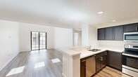 This contemporary two-floor residence is thoughtfully designed with clean lines, bright white walls, and warm wood-tone flooring throughout, creating a cohesive and inviting atmosphere. The open-concept main living area seamlessly connects the kitchen, dining, and living spaces, all bathed in natural light from a sliding glass door that leads to a private balcony. The well-appointed kitchen is a standout feature, boasting dark espresso cabinetry, sleek quartz countertops, stainless steel appliances including a refrigerator, range, microwave, and dishwasher, along with a peninsula with an undermount sink that doubles as additional prep and seating space. The bedrooms are generously sized with large windows that invite natural light; one features mirrored closet doors, while another is served by a spacious walk-in closet with built-in shelving. Two full bathrooms are finished with wood-look flooring, white vanities, and clean modern fixtures — one featuring a tub-shower combo with glass sliding doors. A notable highlight is the private rooftop deck, offering open-air space with panoramic views of surrounding greenery and distant hills under an expansive sky — ideal for outdoor relaxation and entertaining.