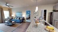 This single-floor, 2-bedroom, 2-bathroom residence offers a well-designed open-concept layout that seamlessly connects the kitchen, dining, and living areas. The kitchen is appointed with granite countertops, a stainless steel sink, and elegant pendant lighting that hangs above the island, creating a functional yet stylish centerpiece for the space. The flooring throughout the main living area features wood-style planks that add warmth and continuity.

The living area is generously proportioned, providing ample room for comfortable furnishings. Neutral wall tones complement the space's coastal-inspired aesthetic, allowing for versatile decorating possibilities. A visible bedroom off the main living area showcases carpeted flooring and a thoughtful layout, offering a private retreat within the residence.

The open sightlines throughout the main living spaces enhance the sense of flow and connectivity. Recessed ventilation, modern lighting fixtures, and clean architectural lines contribute to a polished, contemporary feel. The overall ambiance is bright and welcoming, making this residence a comfortable and functional living environment suited for everyday living.