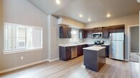 Located at 12501 West 6th Avenue in Airway Heights, Washington, this single-floor unit offers a thoughtfully designed open-concept layout with contemporary finishes throughout. The living area is a standout feature, boasting soaring vaulted ceilings with clerestory windows that flood the space with natural light, complemented by light-toned hardwood-style flooring that flows seamlessly throughout the unit. A sliding glass door opens to a private balcony, extending the living space outdoors.

The kitchen is well-appointed with rich, dark wood cabinetry, white countertops, and a full suite of stainless steel appliances including a refrigerator, electric range, microwave, and dishwasher. A central island provides additional workspace and casual seating. Recessed lighting and a window above the sink add both function and brightness to the space.

The bathroom features light hardwood-style flooring, a dark wood vanity with white countertop, a large mirror, and a full-size tub and shower combination with clean white surround and chrome fixtures.

A dedicated in-unit laundry closet houses a stacked front-loading washer and dryer, adding everyday convenience. The unit also features a wall-mounted mini-split system for efficient climate control. Neutral gray walls and clean architectural lines give the space a modern, move-in-ready appeal.