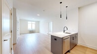 Located at 20 Grand Ave in Englewood, NJ, this thoughtfully designed two-bedroom, two-bathroom residence offers a clean, modern aesthetic across a well-appointed single floor. The open-concept kitchen and living area serves as the heart of the home, featuring light hardwood flooring, sleek blue-gray cabinetry, quartz countertops, a waterfall island with an undermount sink and matte black faucet, stainless steel appliances, and stylish pendant lighting — all complemented by a warm wood accent wall. The living area is bright and airy, bathed in natural light from large windows with city views. Both bedrooms continue the light hardwood flooring and neutral palette, with windows offering urban rooftop views and individual climate control units. The generously sized primary bedroom includes ample closet space. Three closets throughout the residence provide excellent storage. Both bathrooms are finished with large-format tile flooring, floating walnut vanities, LED-backlit mirrors, and matte black fixtures; one bath features a full soaking tub with marble-style tile surround. A connecting hallway ties the layout together efficiently, creating a cohesive and functional living environment.